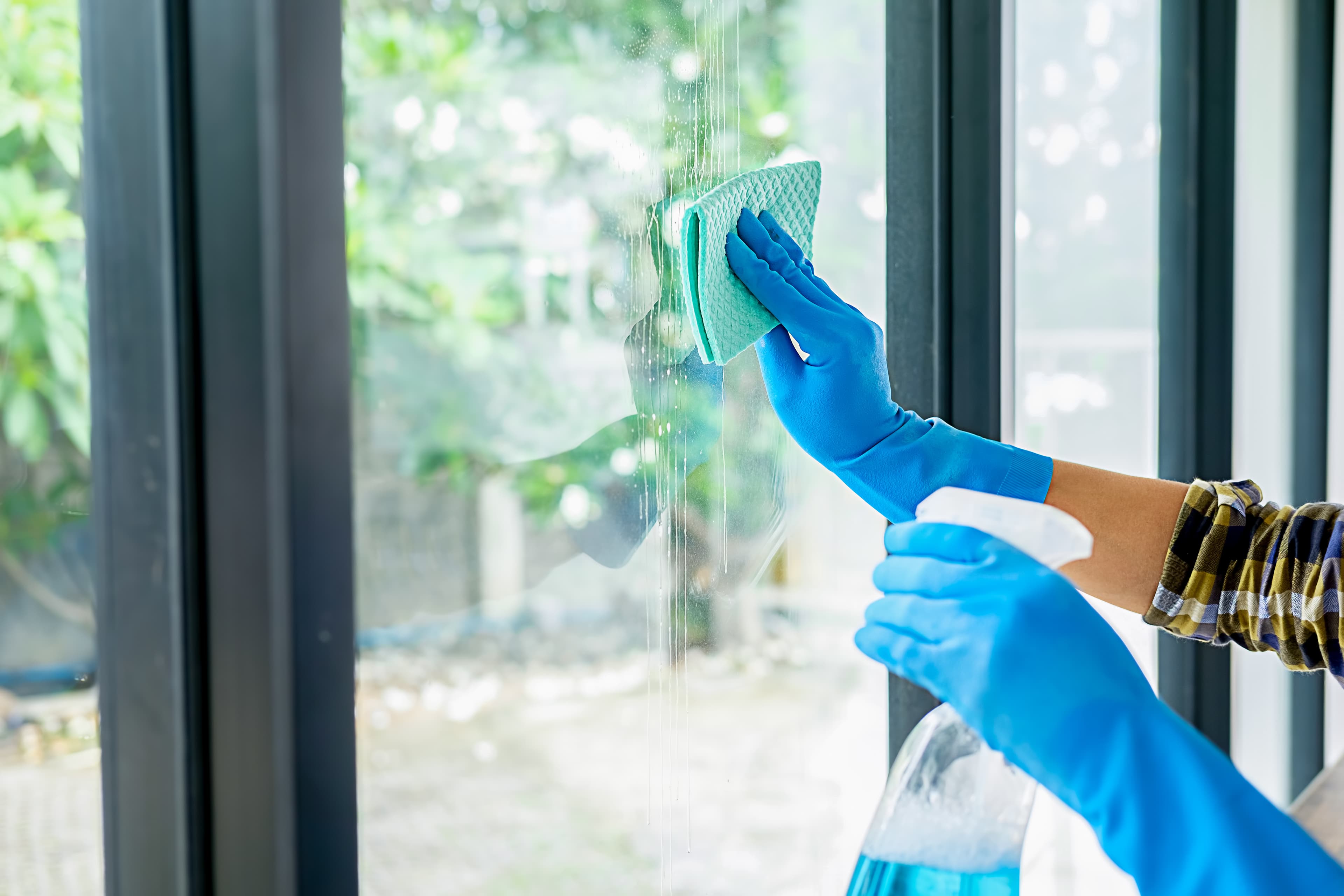 Hands with blue gloves cleaning a residential glass window